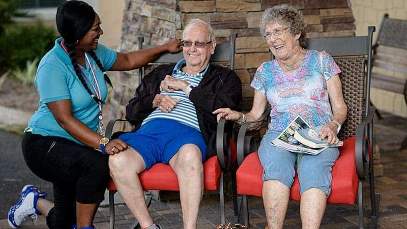 Senior couple seated on patio with staff member kneeling beside them